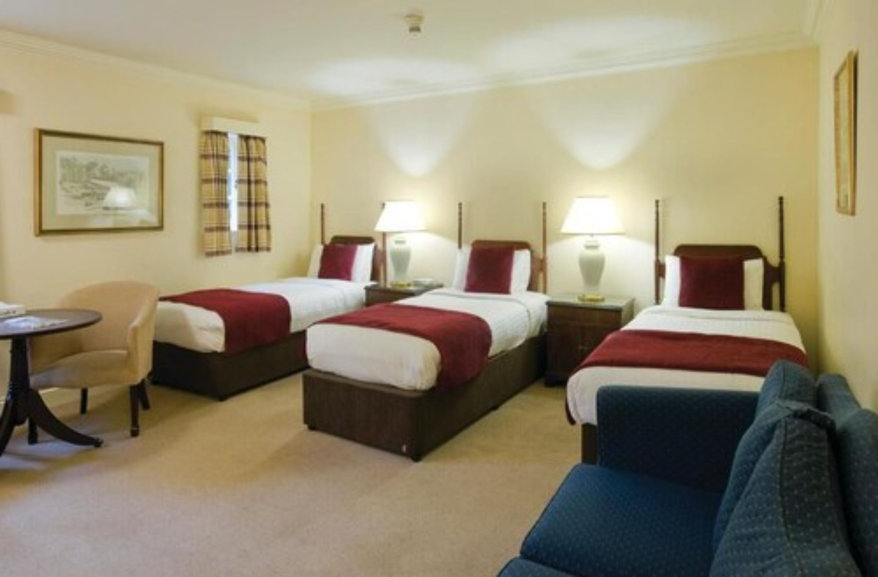 Una habitación de hotel con tres camas, un sofá, una mesita y una silla.