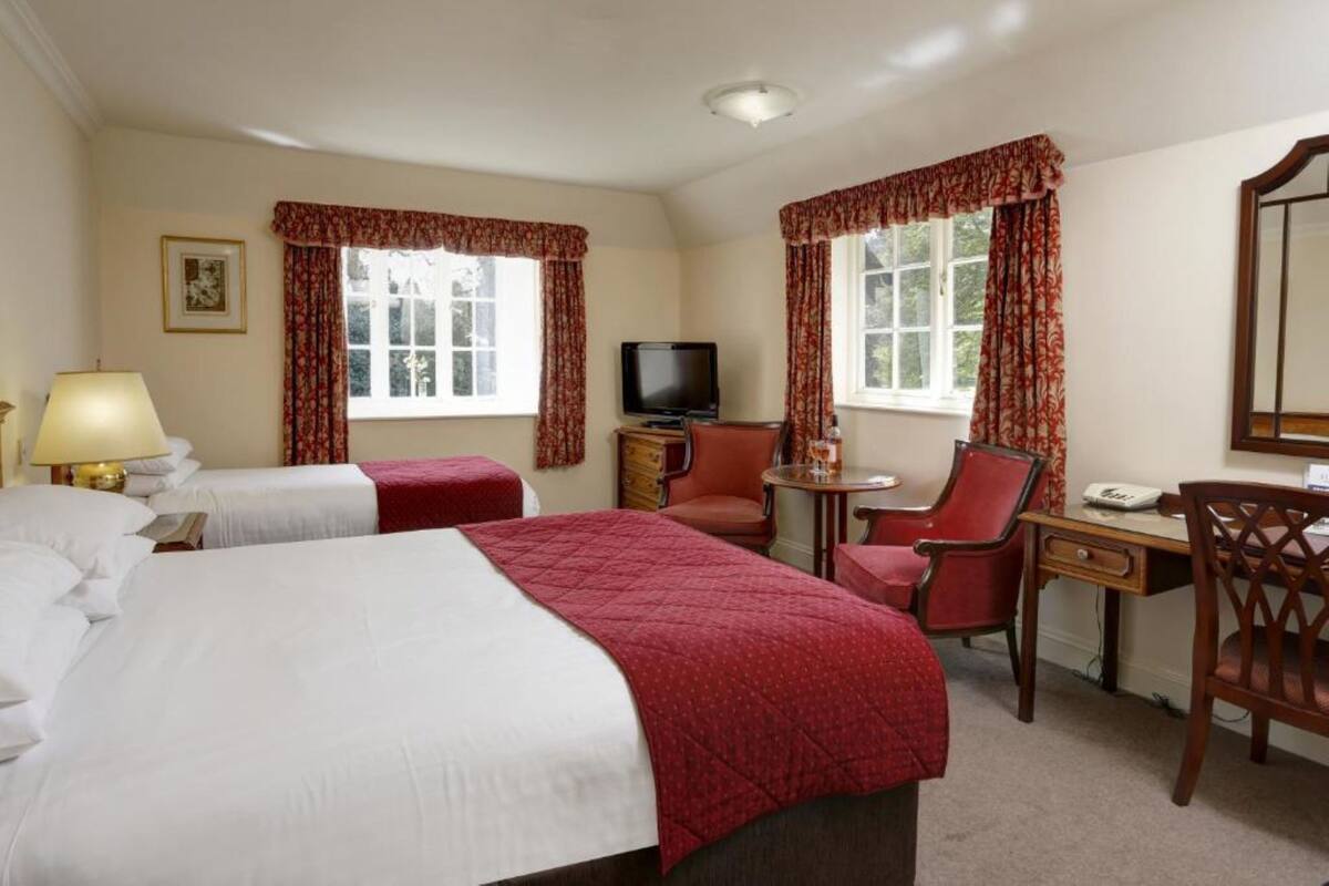 A hotel room with a large bed, two smaller beds, a desk with a chair, a television, and a window with curtains.
