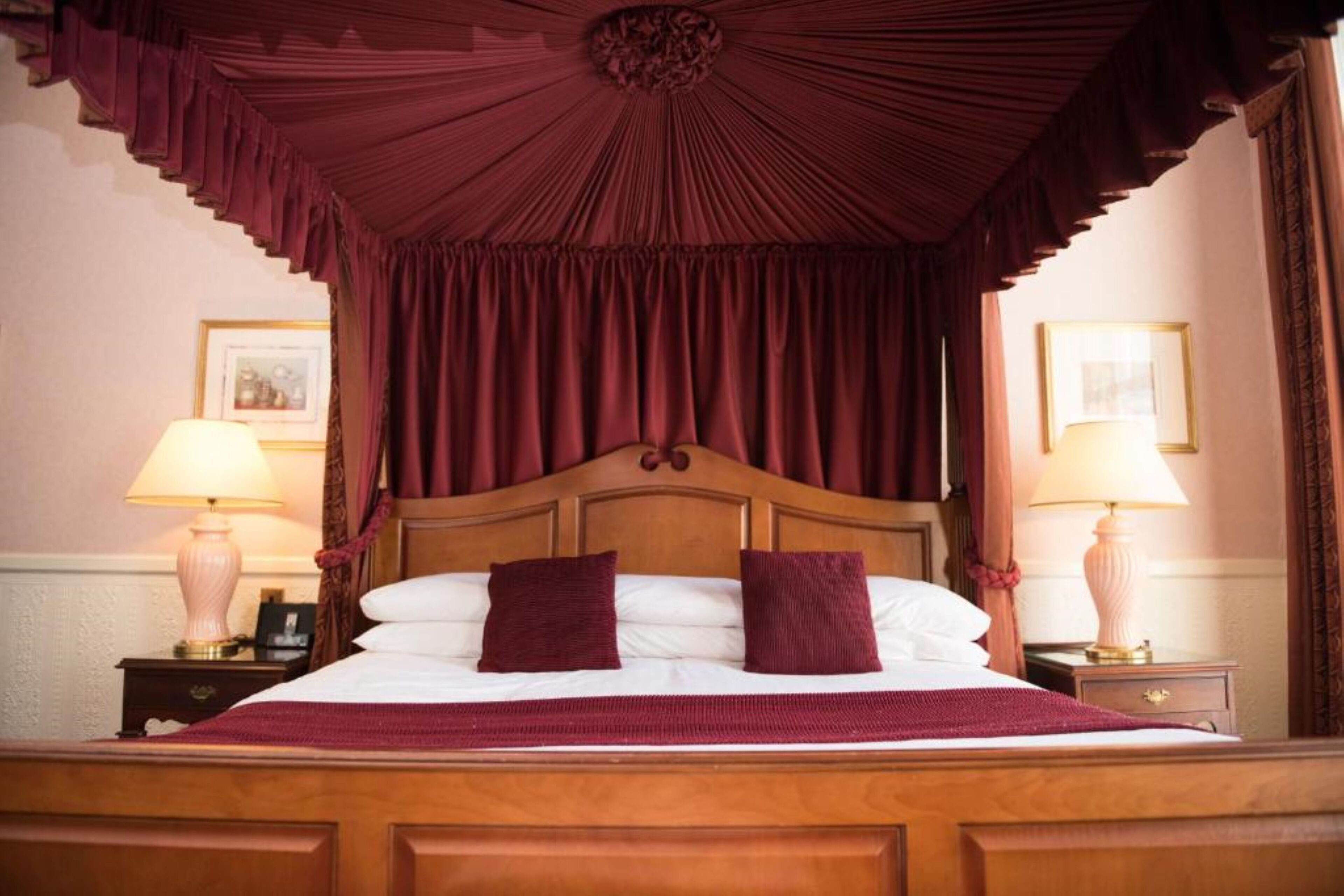 Un lit avec une tête de lit en bois, deux oreillers et une couverture rouge. Il y a deux tables de chevet avec des lampes.