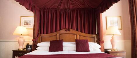 Un lit avec une tête de lit en bois, deux oreillers et une couverture rouge. Il y a deux tables de chevet avec des lampes.