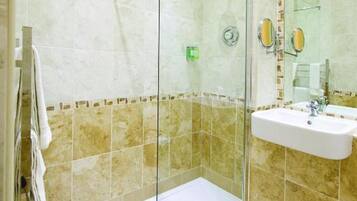 Un baño moderno con ducha envuelta en vidrio, un lavabo blanco y azulejos color beige.
