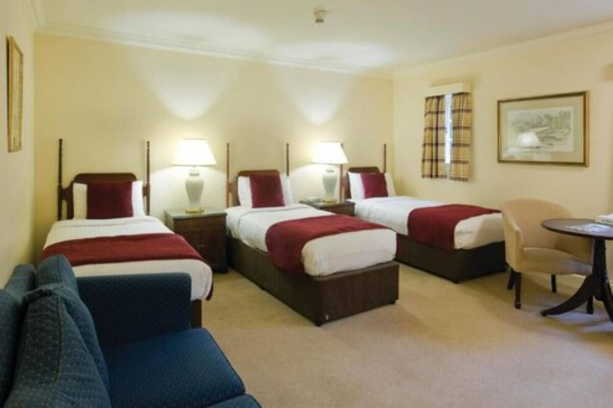 A hotel room with three single beds, a small round table, a chair, and a sofa.