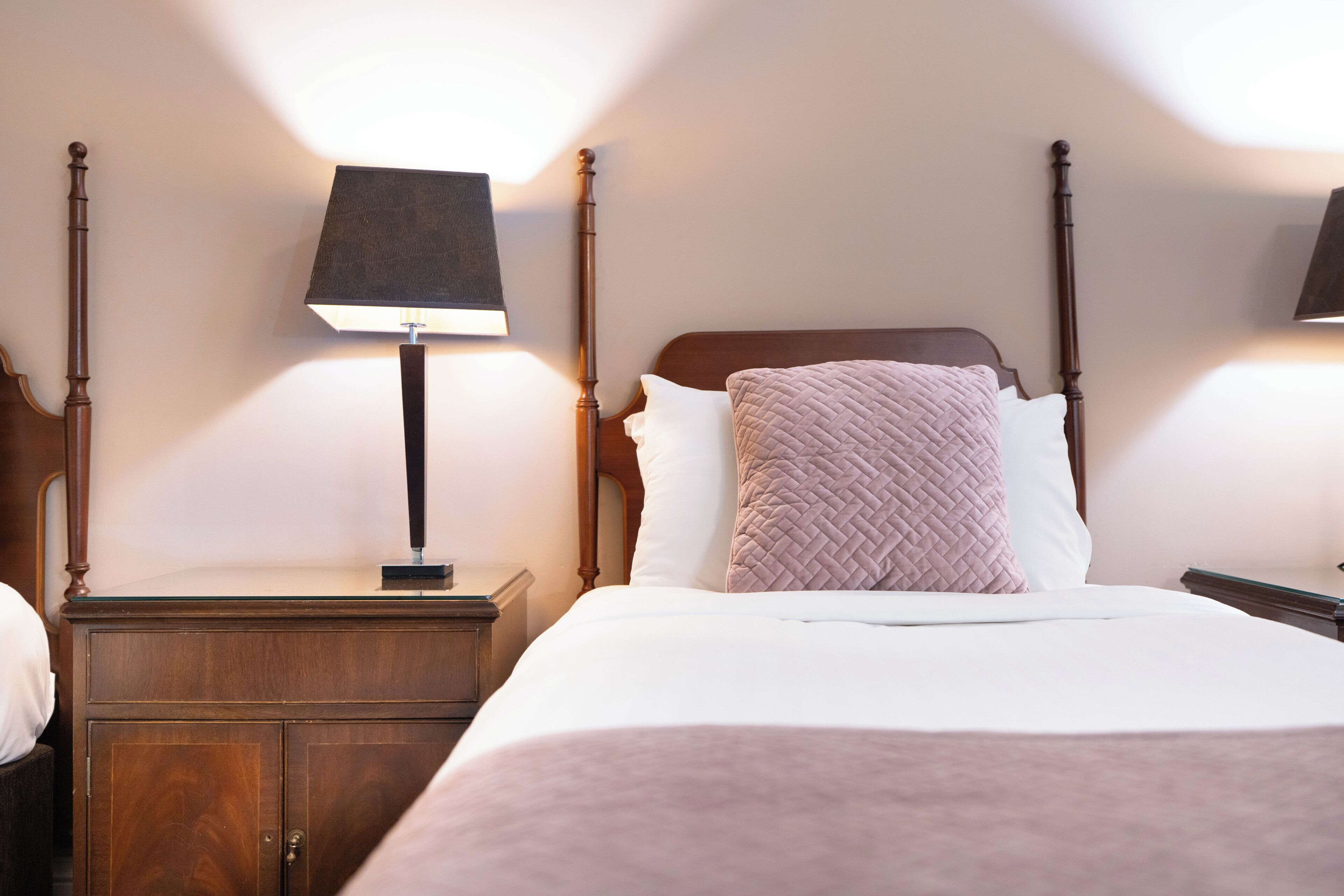 Ein ordentlich bezogenes Bett mit hölzernem Kopfteil, einem Nachttisch mit Lampe und einem zusätzlichen Holzbeistelltisch.
