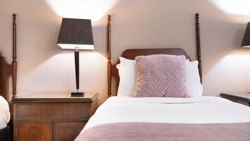 Ein ordentlich bezogenes Bett mit hölzernem Kopfteil, einem Nachttisch mit Lampe und einem zusätzlichen Holzbeistelltisch.
