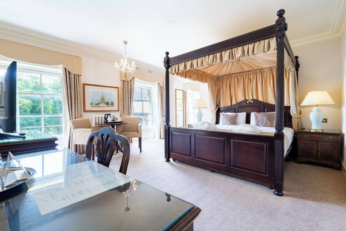 A four-poster bed with a canopy, a television, a dining table with chairs, and a desk with a chair.