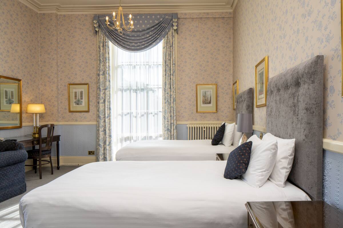A hotel room with two beds, a desk, and a chair.
