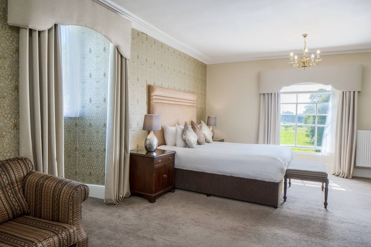 A bedroom with a large bed, a nightstand, a chair, and a window with curtains.