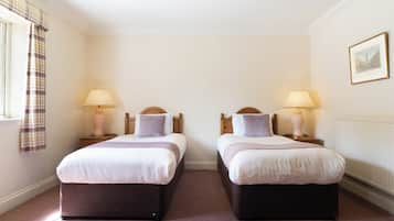 Una habitación con dos camas, cada una con una mesita de noche y una lámpara. La habitación tiene una ventana con cortinas y un cuadro en la pared.