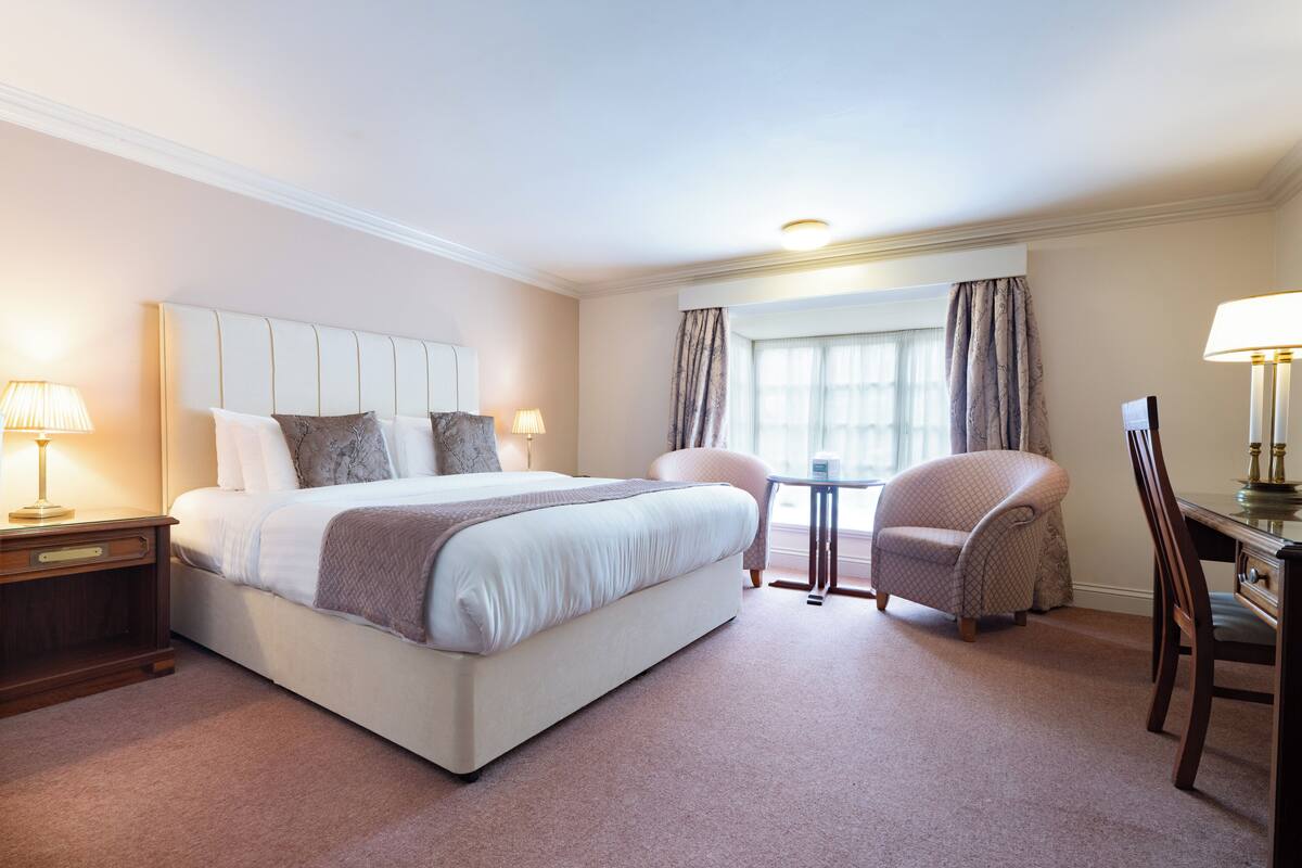 A hotel room with a large bed, a desk, a chair, and a window with curtains.