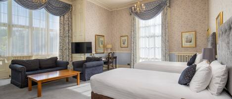 A hotel room with two beds, a sofa, a desk, and a television.