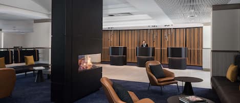 A modern lounge area with leather sofas, a central fire feature, and a wooden panel wall.