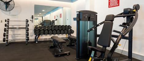 A gym with weightlifting equipment, a bench, and a fan.