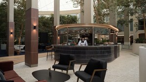 A modern bar area with a curved counter, seating with black and wooden chairs, and a high ceiling with natural light. - Rydges Canberra (Forrest)