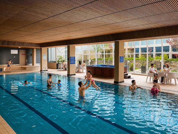 Una piscina interior con agua cristalina, rodeada por una zona cubierta con asientos y vistas al exterior.