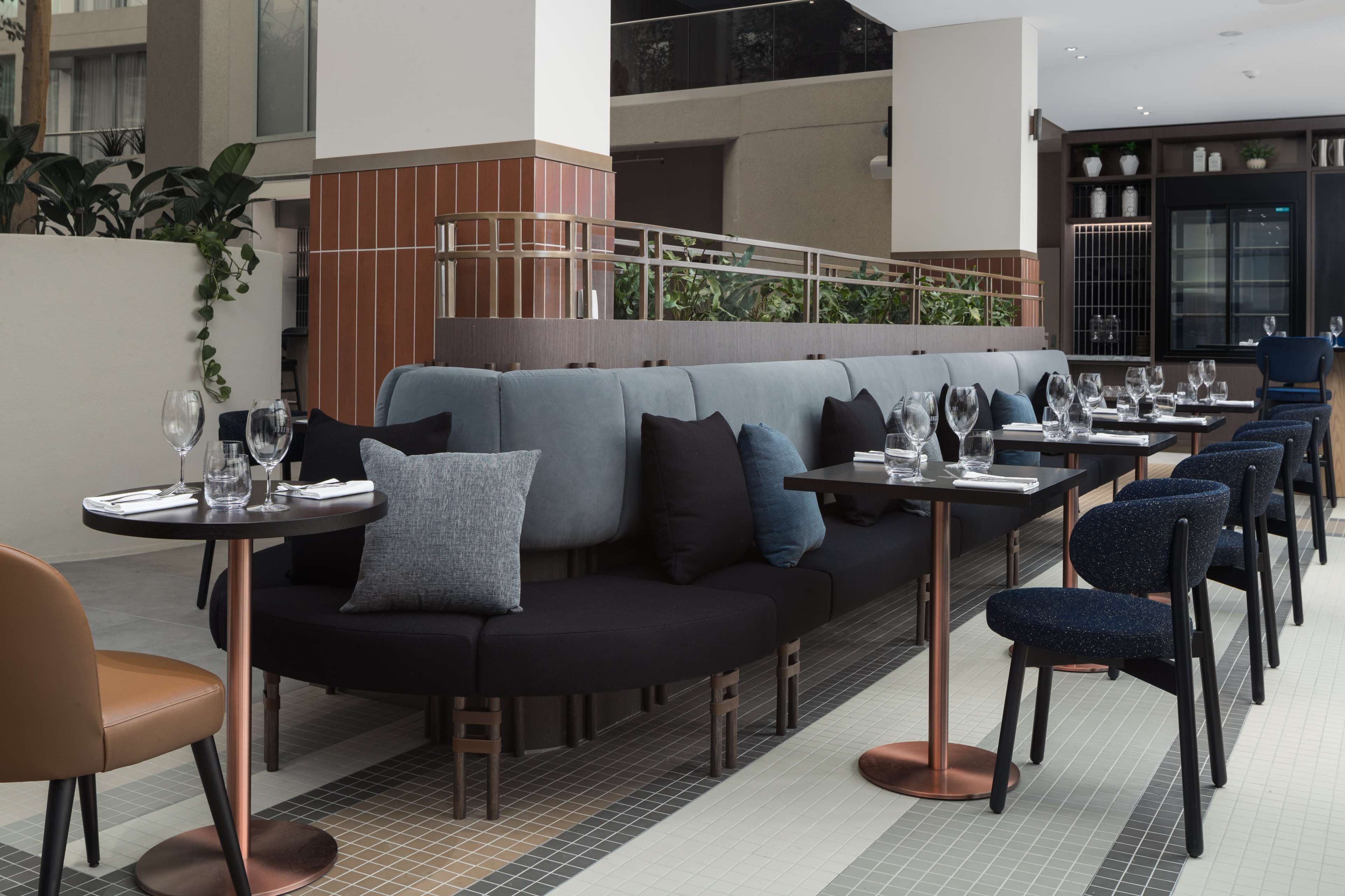 A modern restaurant with a long counter, cushioned seating, and a tiled floor.