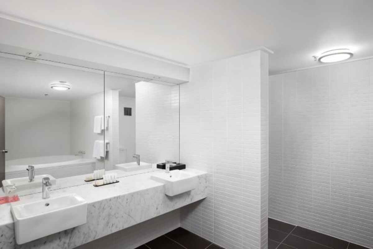 A modern bathroom with a large mirror, two sinks, and a shower area.