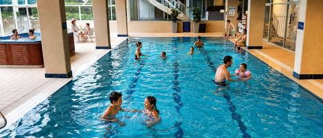 Une piscine intérieure à l’eau claire, entourée d’un sol carrelé et surmontée d’un plafond en bois.