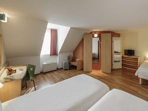 Una habitación de hotel moderna con techo inclinado, un escritorio con silla, cama, televisor y armario.