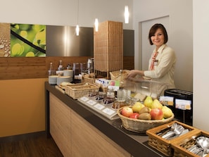 Ein Buffet mit verschiedenen Speisen, eine Person bedient den Tresen und ein digitales Menü ist ebenfalls vorhanden.
