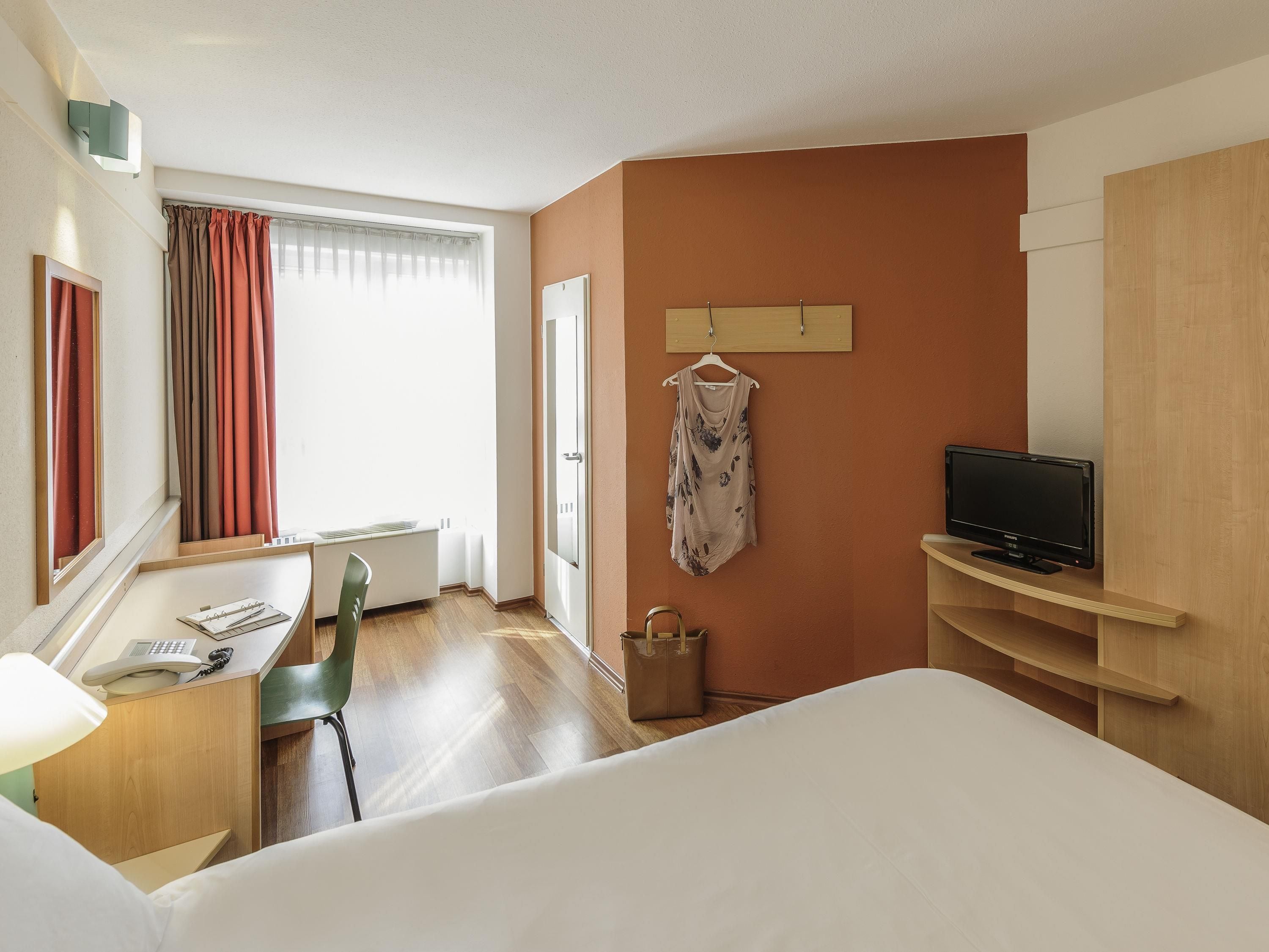 A hotel room with a bed, desk, chair, TV, and a window with curtains.