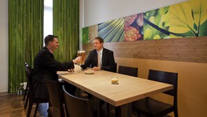 Two people seated at a wooden table in a restaurant with a green curtain backdrop and a large botanical wall mural. - ibis Bamberg Altstadt (Bamberg)