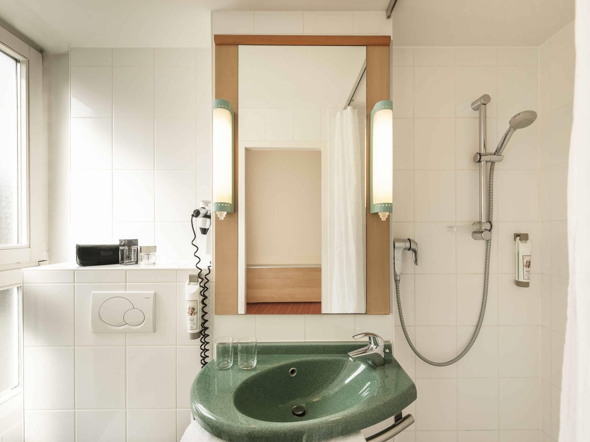 A bathroom with a green sink, a mirror, a shower, and a window.