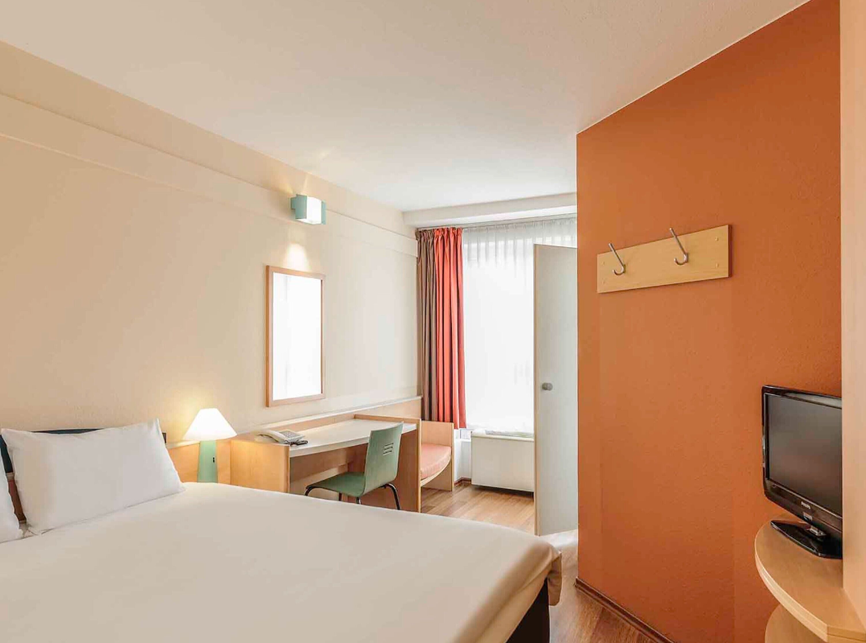 Una habitación de hotel con una cama grande, un escritorio, una silla, un televisor y una ventana con cortinas.