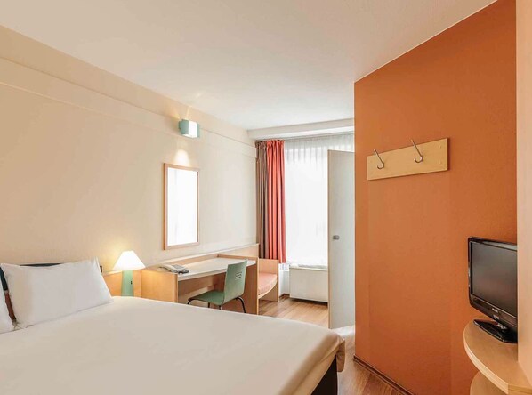 A hotel room with a large bed, a desk, a chair, a television, and a window with curtains.