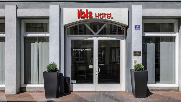 ibis hotel, moderne facade, store glasdøre og to plantekasser ved indgangen.