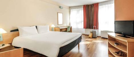 Habitación de hotel con cama, mesitas de noche, escritorio, televisor, maleta y ventana con cortinas.