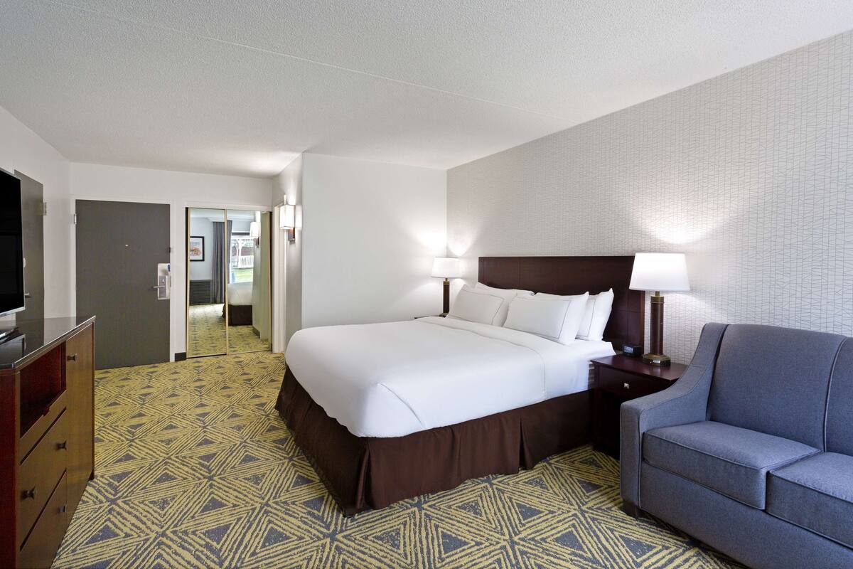 A hotel room with a large bed, a TV, a sofa, and a patterned carpet.