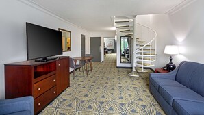 A modern living room with a flat-screen TV, a wooden cabinet, a blue sofa, a patterned carpet, and a spiral staircase leading to another room. - DoubleTree by Hilton Washington Meadow Lands Casino Area (Washington)