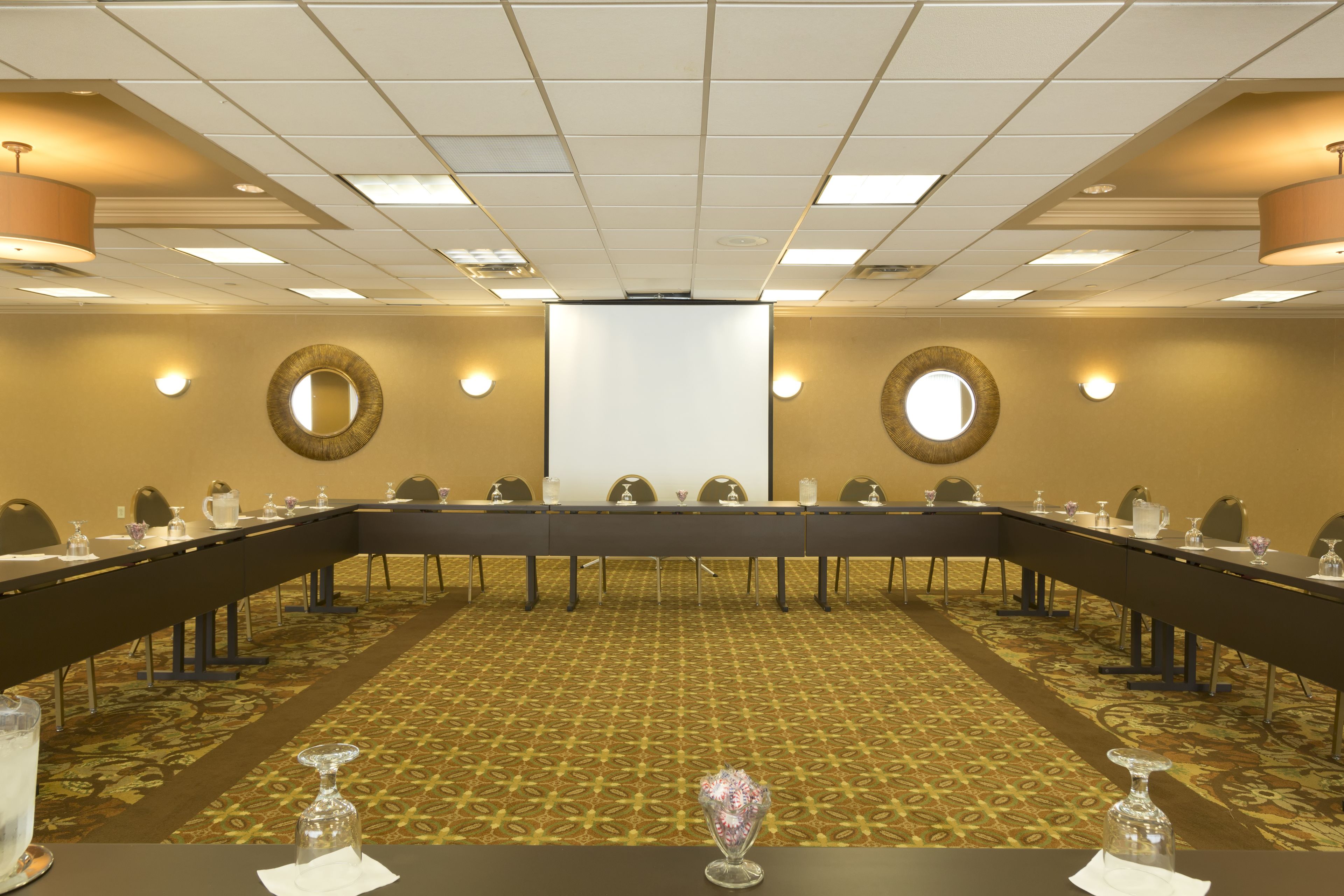 Un salón de conferencias con una larga mesa, sillas y una pantalla para proyector.