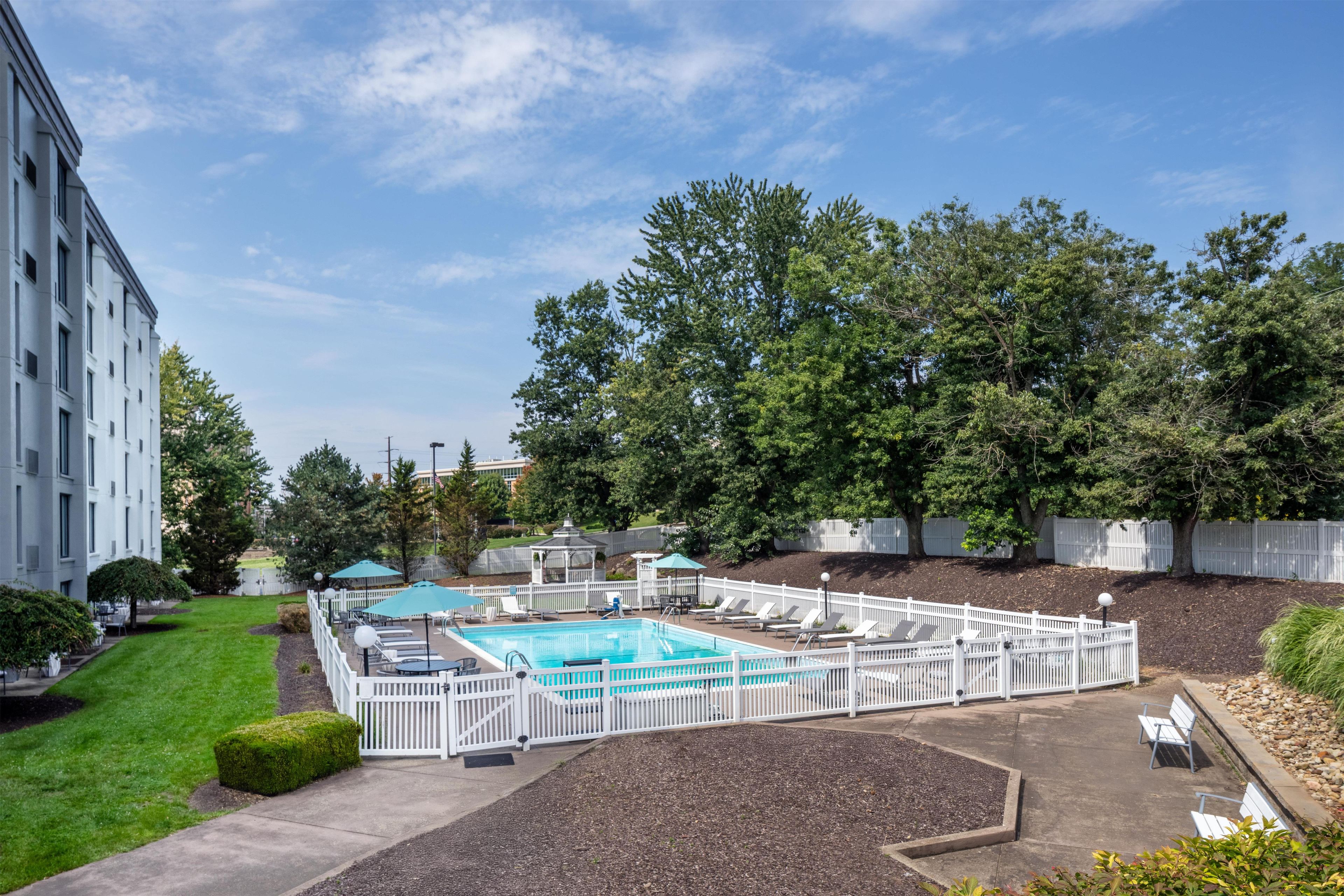 Una piscina rodeada de cercas blancas, con árboles y un edificio al fondo.
