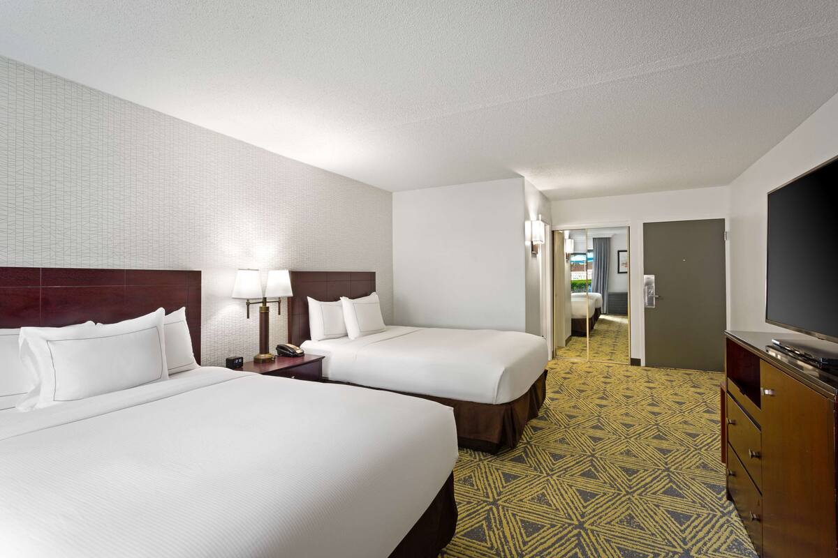 A hotel room with two beds, a television, and a patterned carpet.