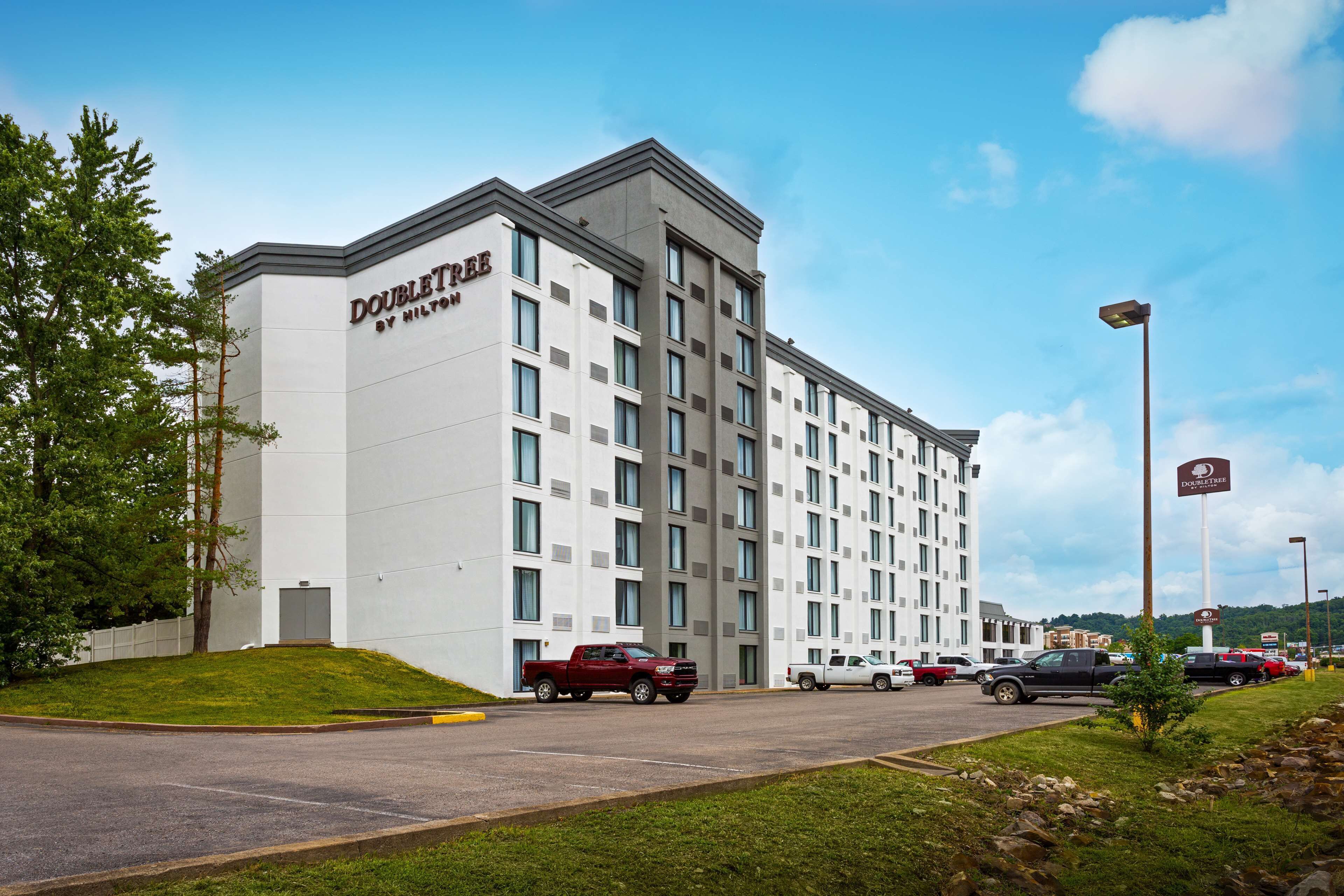 A modern hotel with a flat facade, multiple windows, and a parking lot with several vehicles.