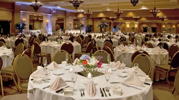 Un salón de banquetes con mesas redondas dispuestas para comer, cada una con mantel blanco, sillas y centros de mesa.