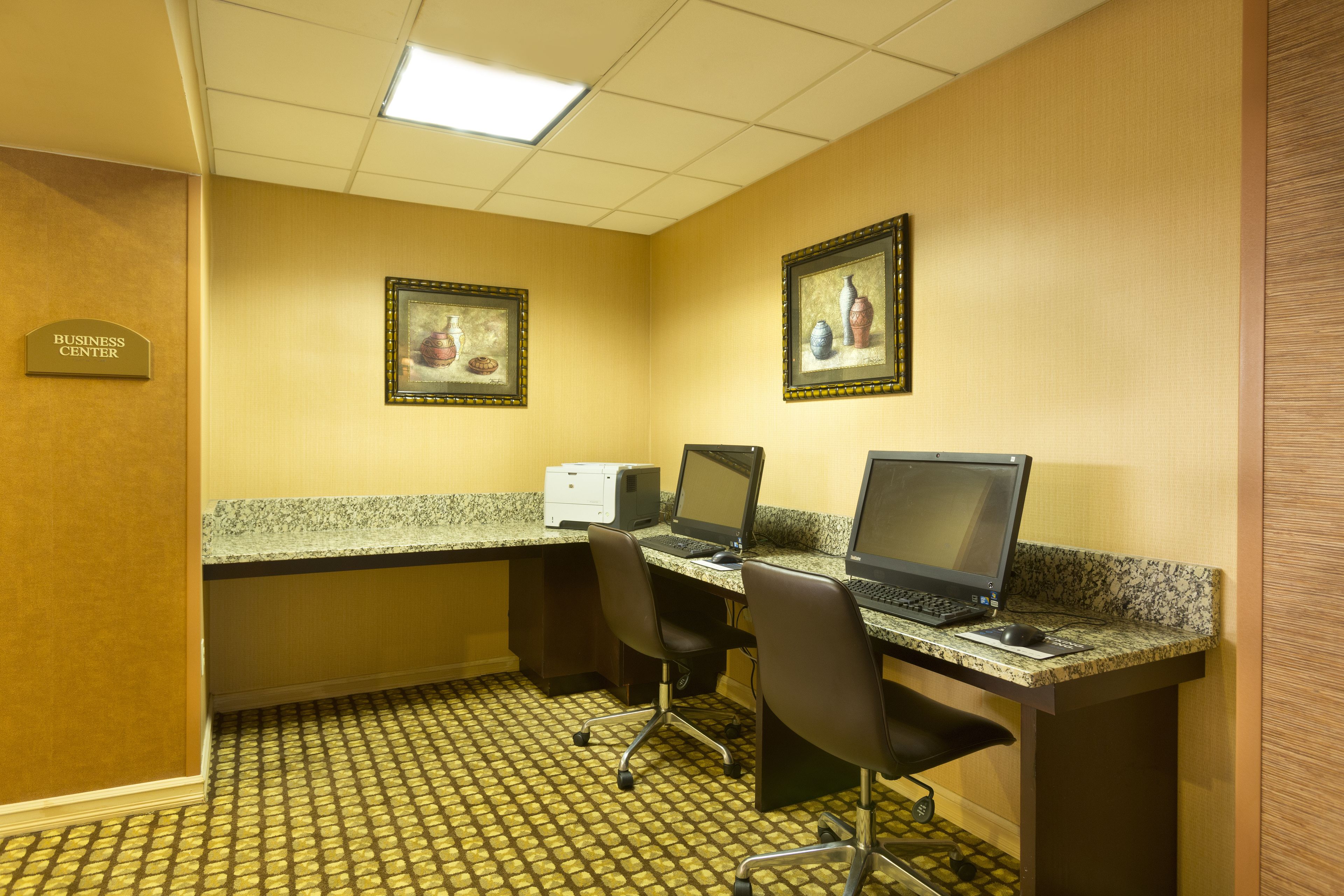 A business center with two desktop computers, a printer, and framed artwork on the walls.