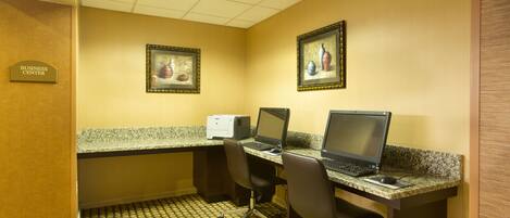A business center with two desktop computers, a printer, and framed artwork on the walls.