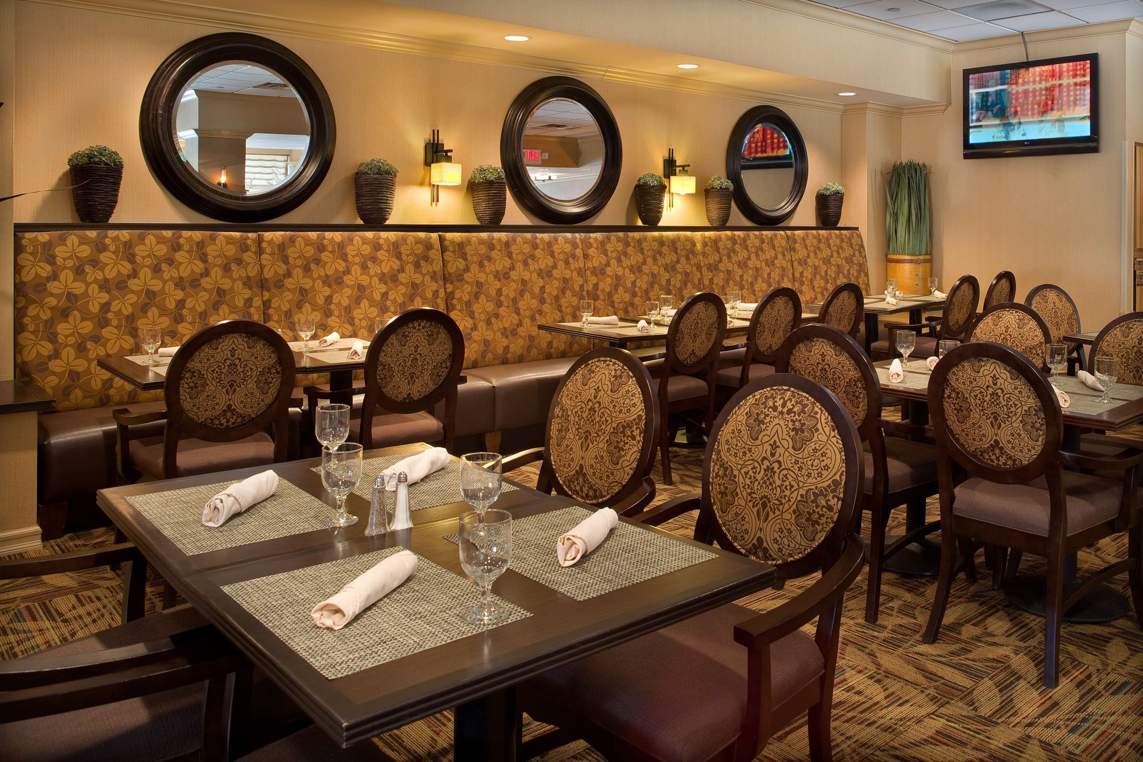 A restaurant with round tables, cushioned booths, and a TV mounted on the wall.
