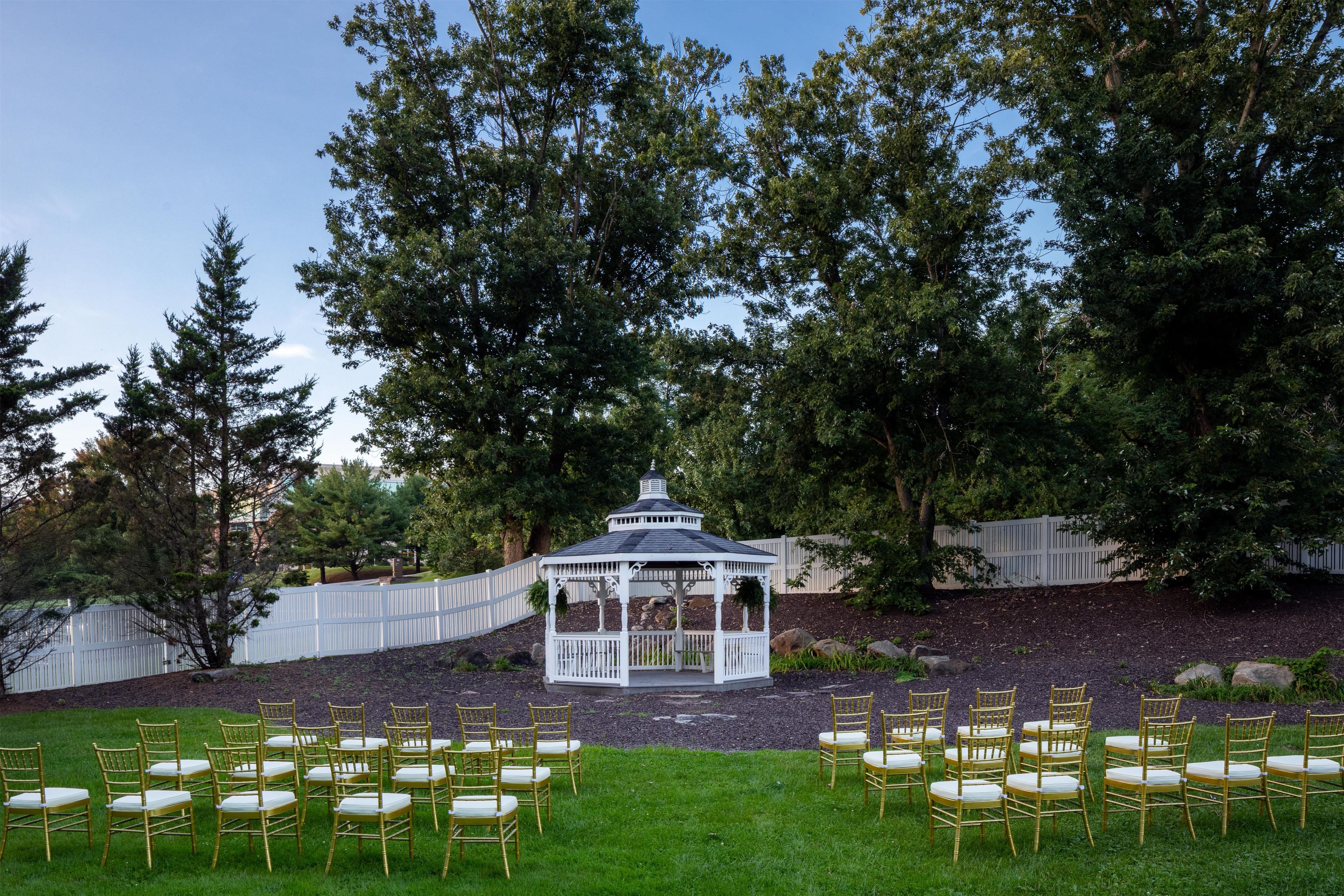 A gazebo with a white fence and chairs arranged in rows on a grassy area.