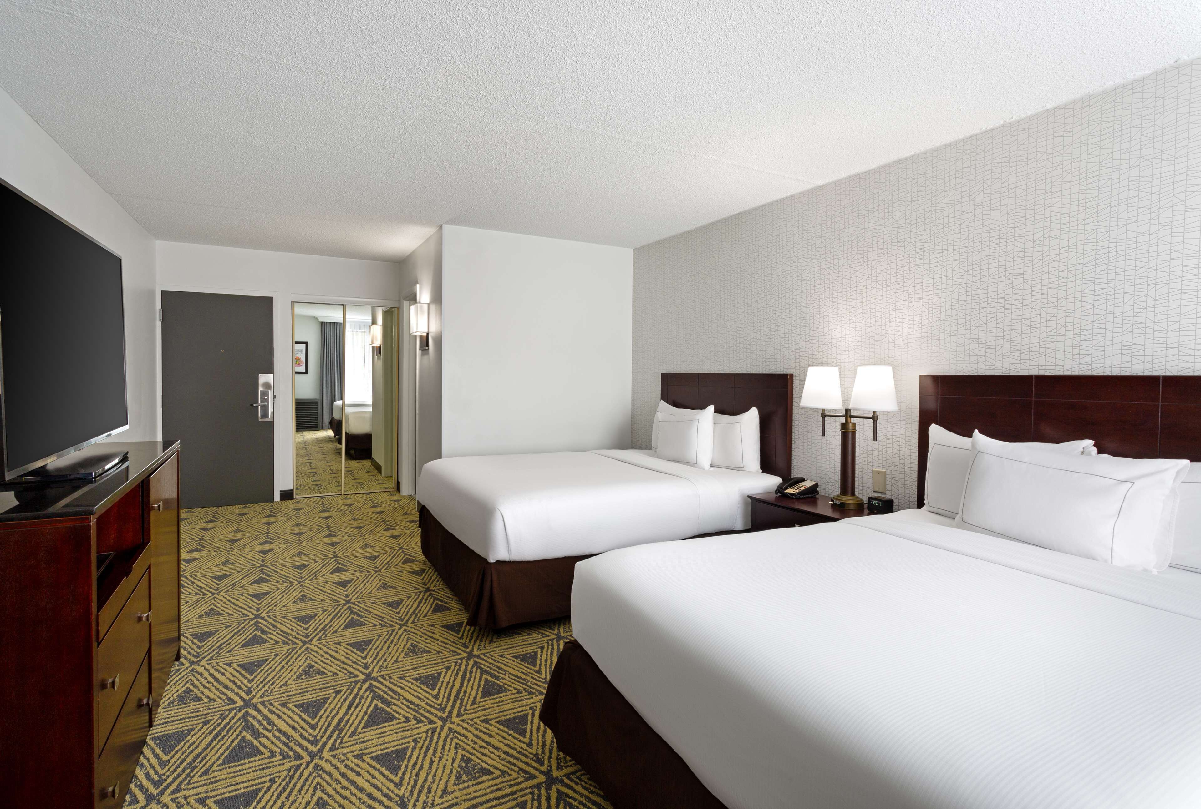 A hotel room with two beds, a desk with a flat-screen TV, and a patterned carpet.