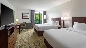 A hotel room with two beds, a desk, a TV, and a view of greenery outside. - DoubleTree by Hilton Washington Meadow Lands Casino Area (Washington)