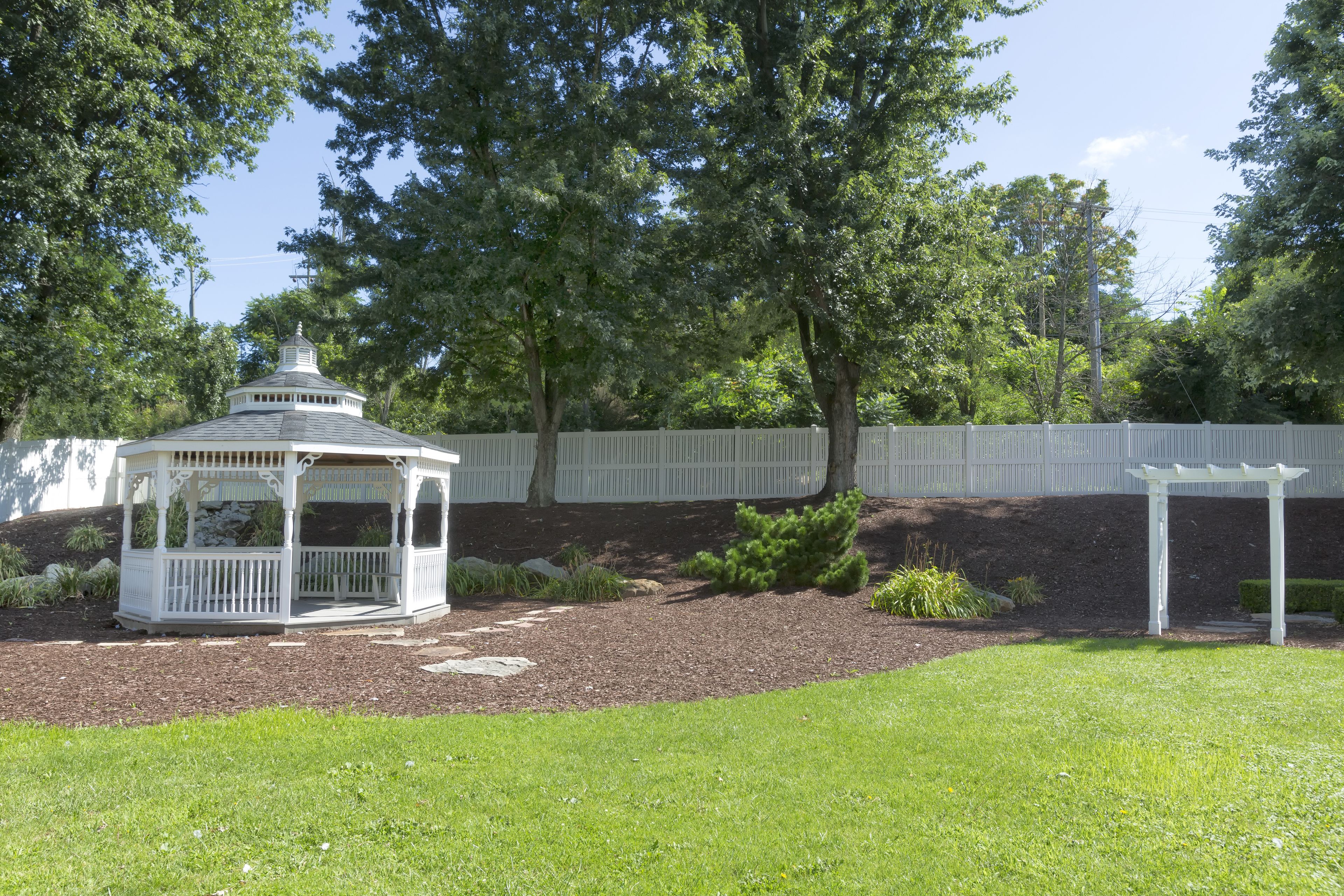 A gazebo with a white fence and trees in the background.
