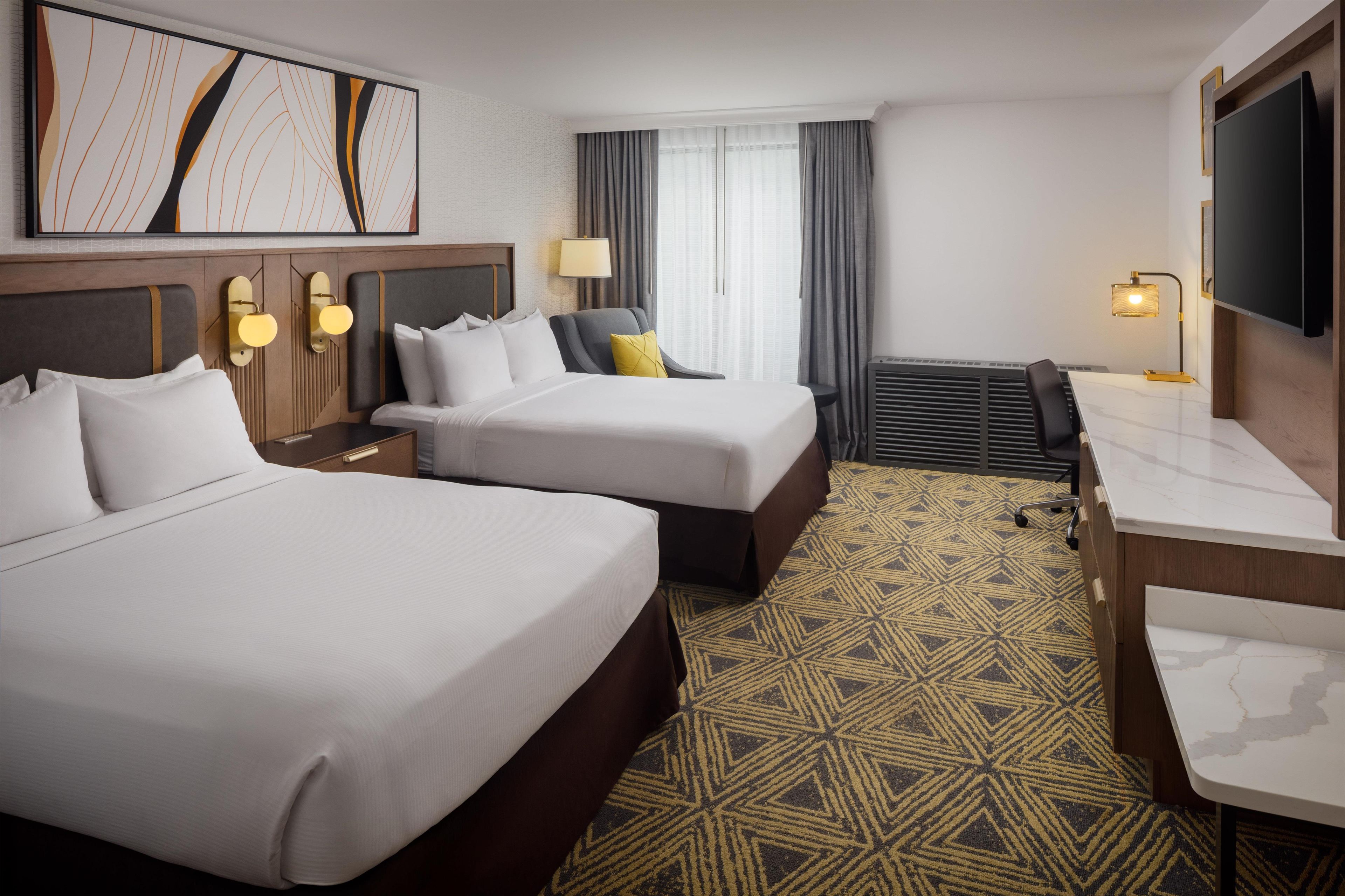Een hotelkamer met twee bedden, een bureau, een stoel, een televisie en een kamer met een patroon.