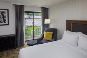 A hotel room with a bed, a chair with a yellow pillow, a small table, and a view of a pool and white fence. - DoubleTree by Hilton Washington Meadow Lands Casino Area (Washington)