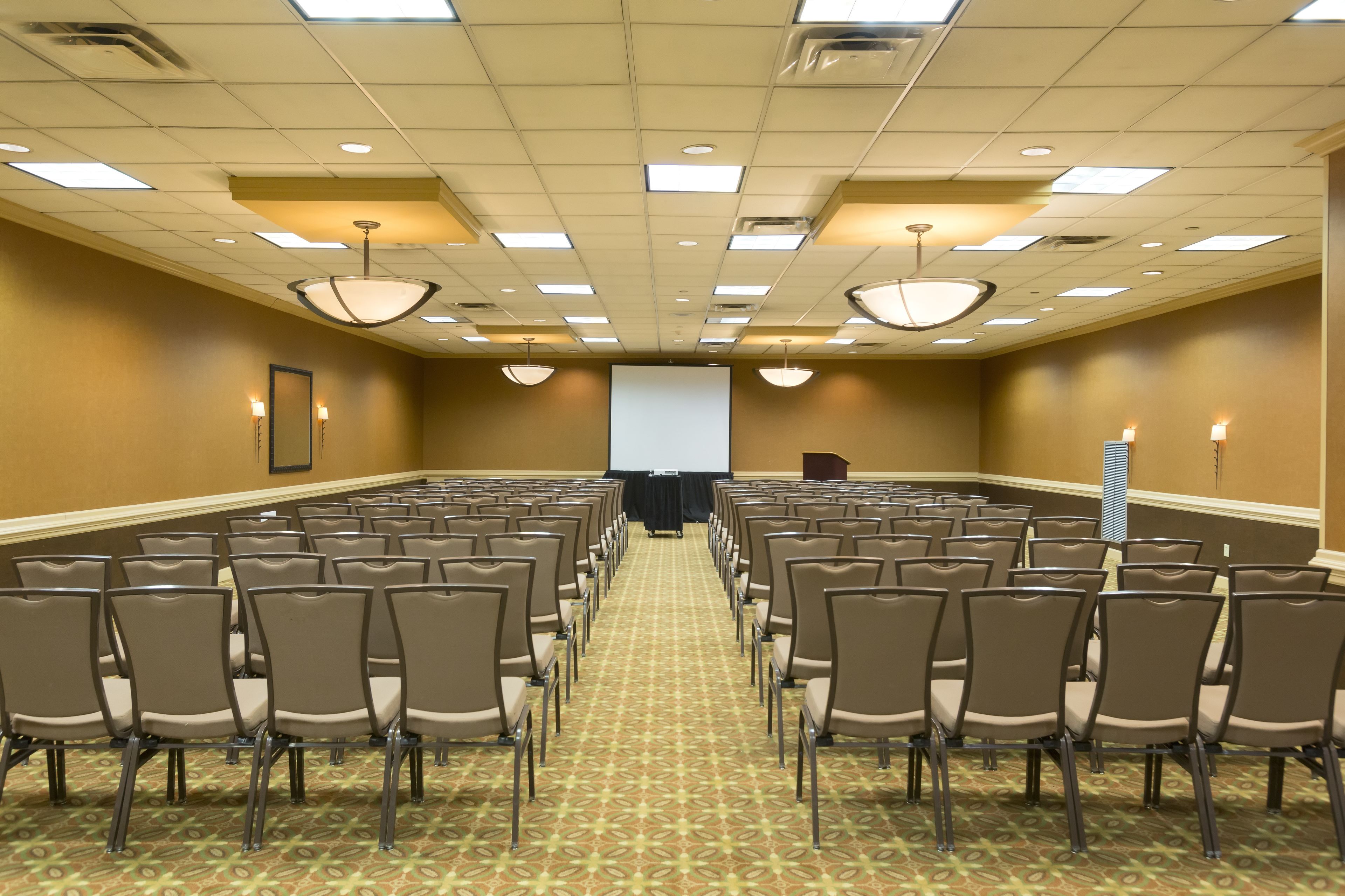 Un salón de conferencias con filas de sillas, una pantalla de proyector y un atril.