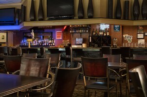 A bar area with multiple seating arrangements, a television mounted on the wall, and various liquor bottles displayed on shelves.