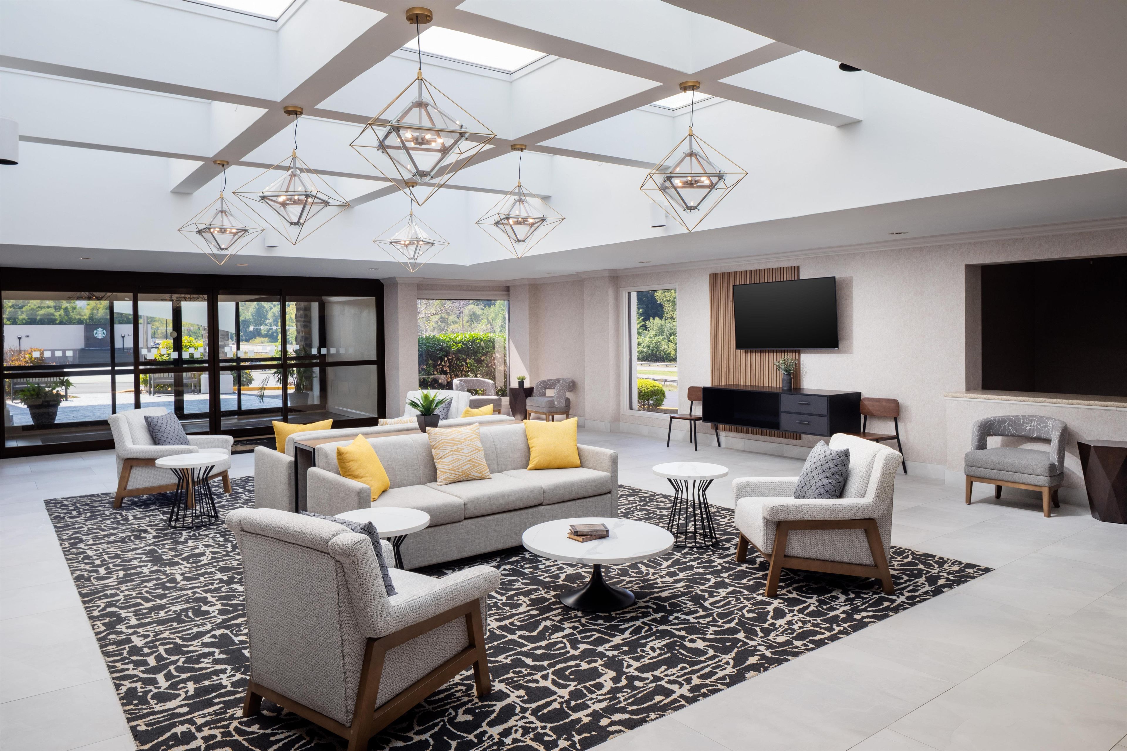 A spacious living area with a high ceiling, modern furniture, and a large window offering a view of the outdoors.