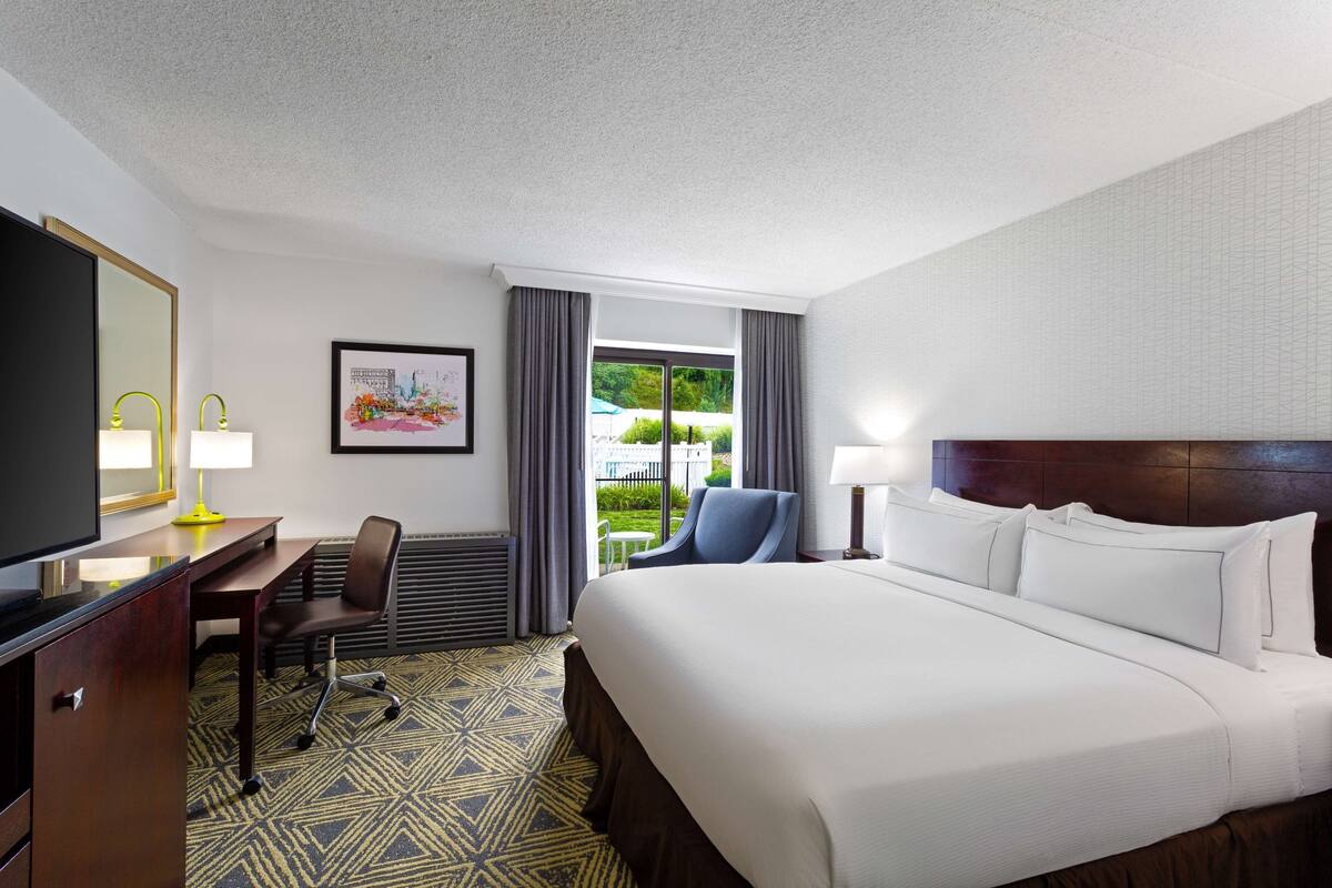 A hotel room with a large bed, a desk with a chair, a television, and a window with curtains.